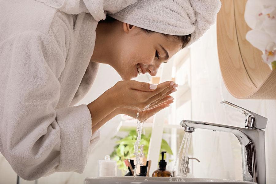 Beautiful teenage girl washing face with cleansing foam in bathroom. Skin care cosmetic