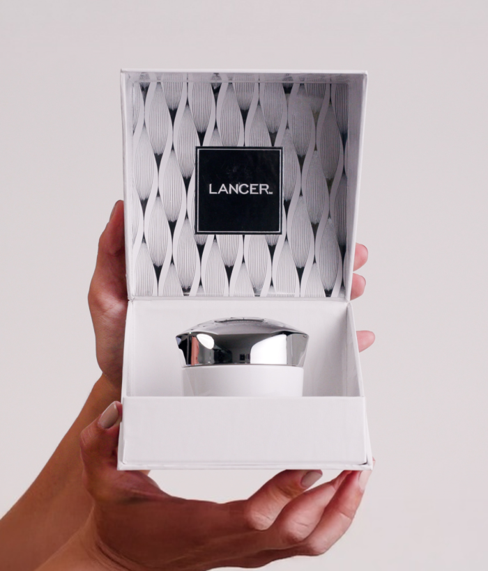 Hand holding a white cosmetic container with 'Lancer' branding against a light background-Lancer Skincare