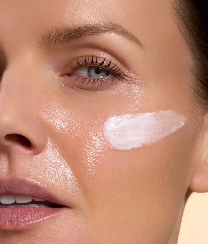 Close-up of a woman's face with a light-colored cream applied to her cheek.-Lancer Skincare
