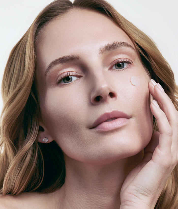 Woman applying cream to her face with a neutral background-Lancer Skincare