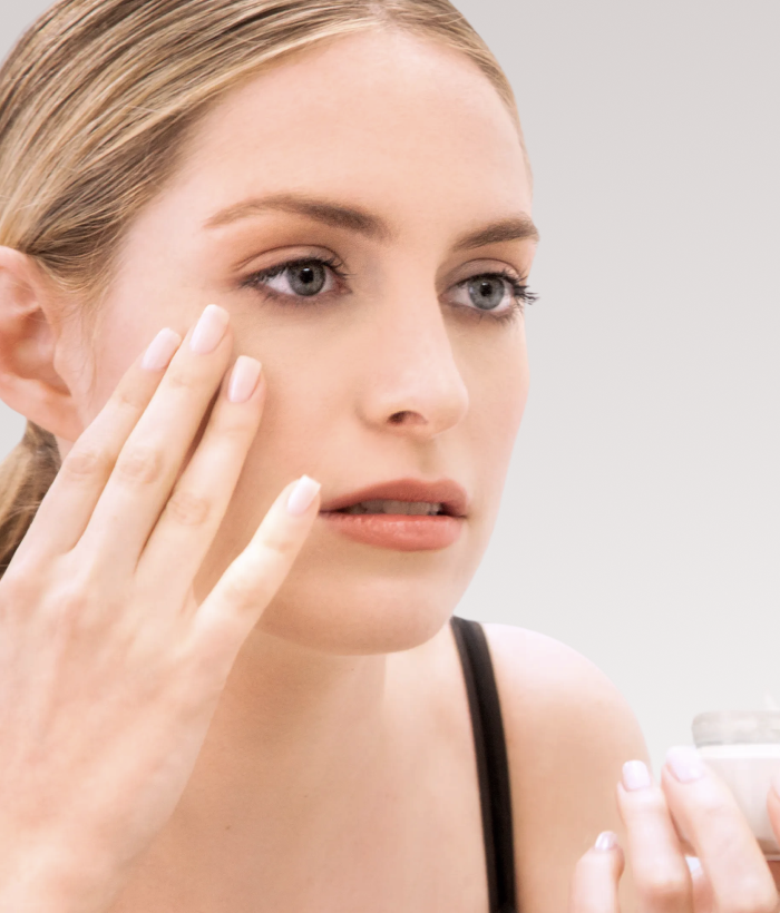 Woman applying cream to her face with a neutral background-Lancer Skincare