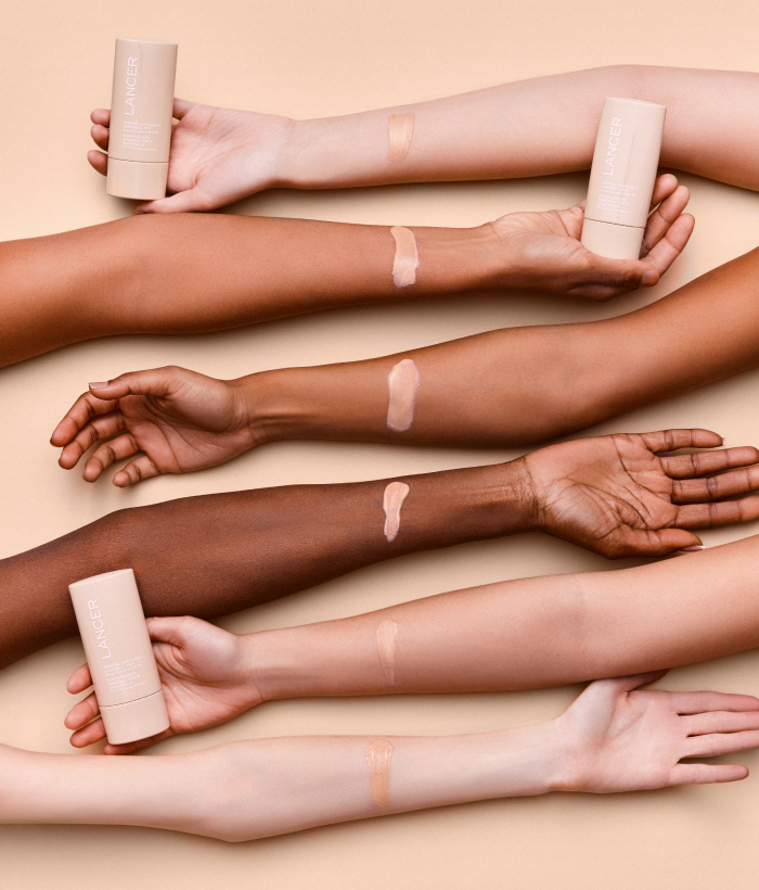 Multiple arms with different skin tones holding a cosmetic product against a beige background-Lancer Skincare